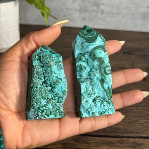 Puede incluir: Dos puntas de cristal de malaquita verde con un patr&oacute;n de remolino. Las puntas miden aproximadamente 5 cm de alto y se sostienen en una mano.