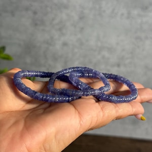 Puede incluir: Tres pulseras de cuentas moradas apiladas una encima de la otra en una mano.