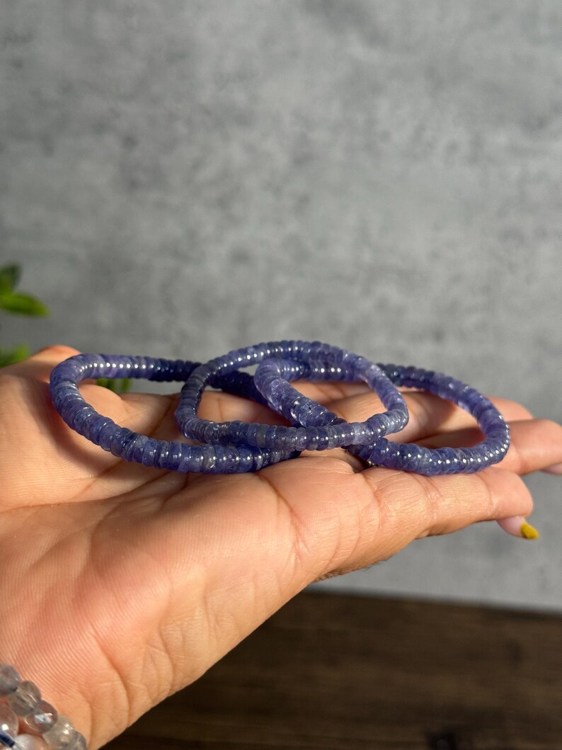 Puede incluir: Tres pulseras de cuentas moradas apiladas una encima de la otra en una mano.
