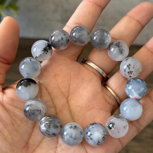 May include: A bracelet made of round, white and gray gemstone beads with black inclusions. The beads are strung on an elastic cord.