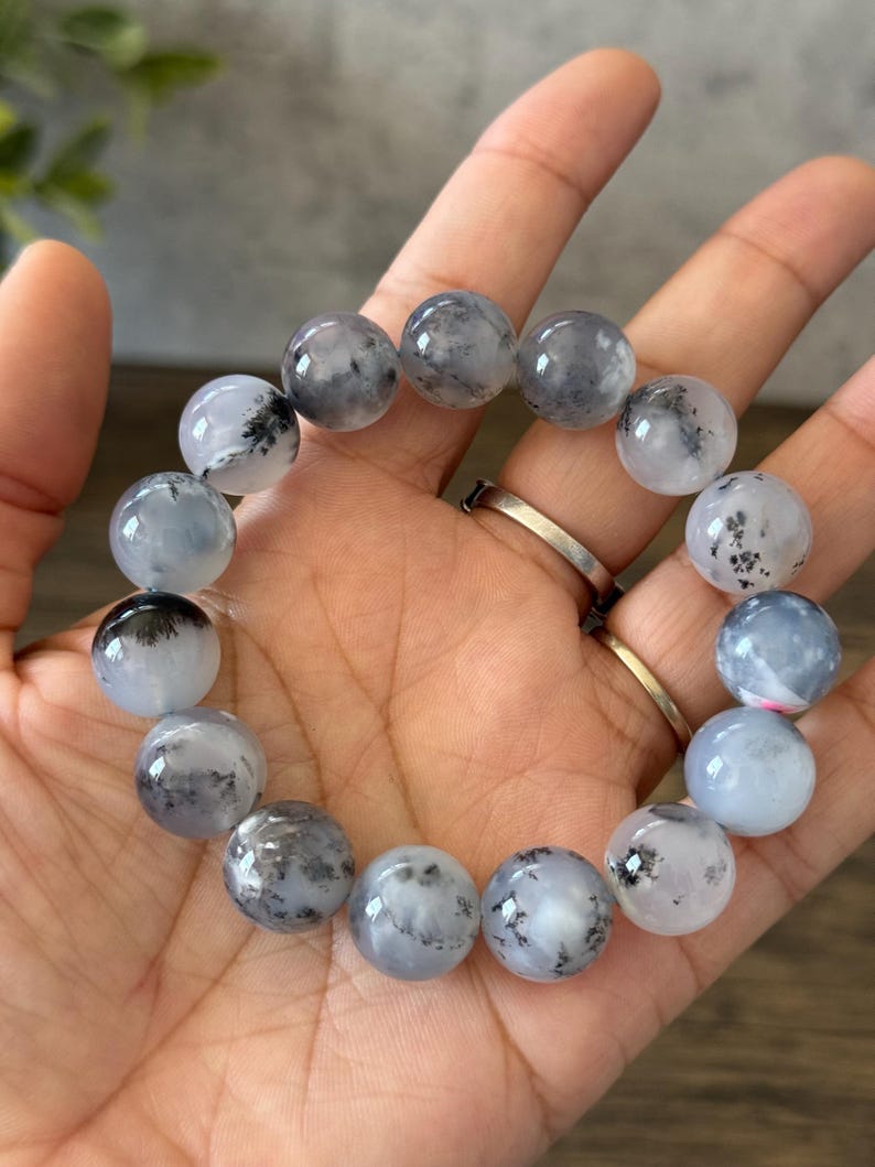 May include: A bracelet made of round, white and gray gemstone beads with black inclusions. The beads are strung on an elastic cord.