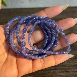 Puede incluir: Un conjunto de cinco pulseras de cuentas de piedras preciosas de color p&uacute;rpura. Las pulseras est&aacute;n hechas con cuentas peque&ntilde;as y redondas y est&aacute;n apiladas unas sobre otras.
