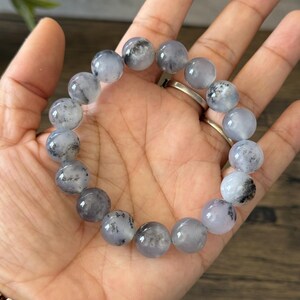 May include: A bracelet made of round, white and gray beads with black flecks. The beads are strung on a clear elastic cord.