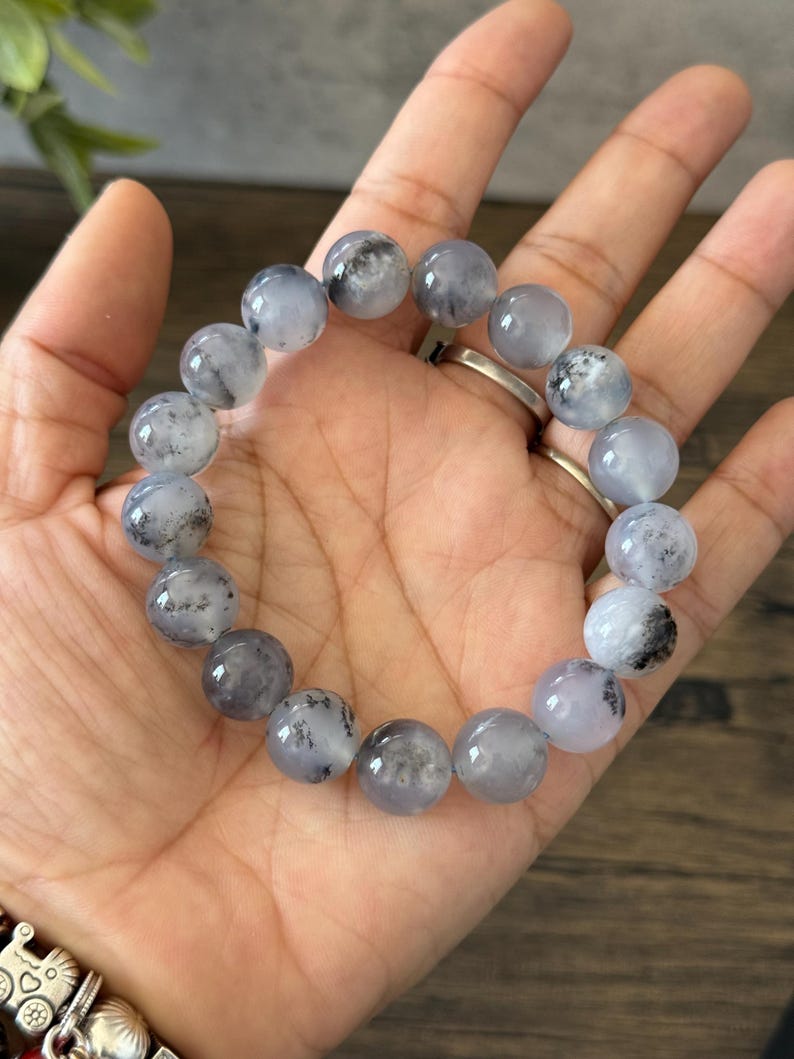 May include: A bracelet made of round, white and gray beads with black flecks. The beads are strung on a clear elastic cord.