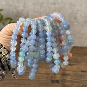 Puede incluir: Una pila de pulseras de cuentas de &aacute;gata azul y verde. Las pulseras est&aacute;n hechas con cuentas redondas y todas son del mismo tama&ntilde;o.