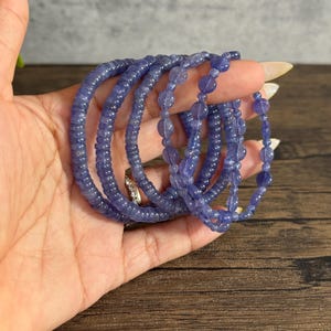 Puede incluir: Un conjunto de seis pulseras de piedras preciosas azules, cada una con un tama&ntilde;o y estilo de cuentas diferente. Las pulseras est&aacute;n apiladas una encima de la otra en una mano.