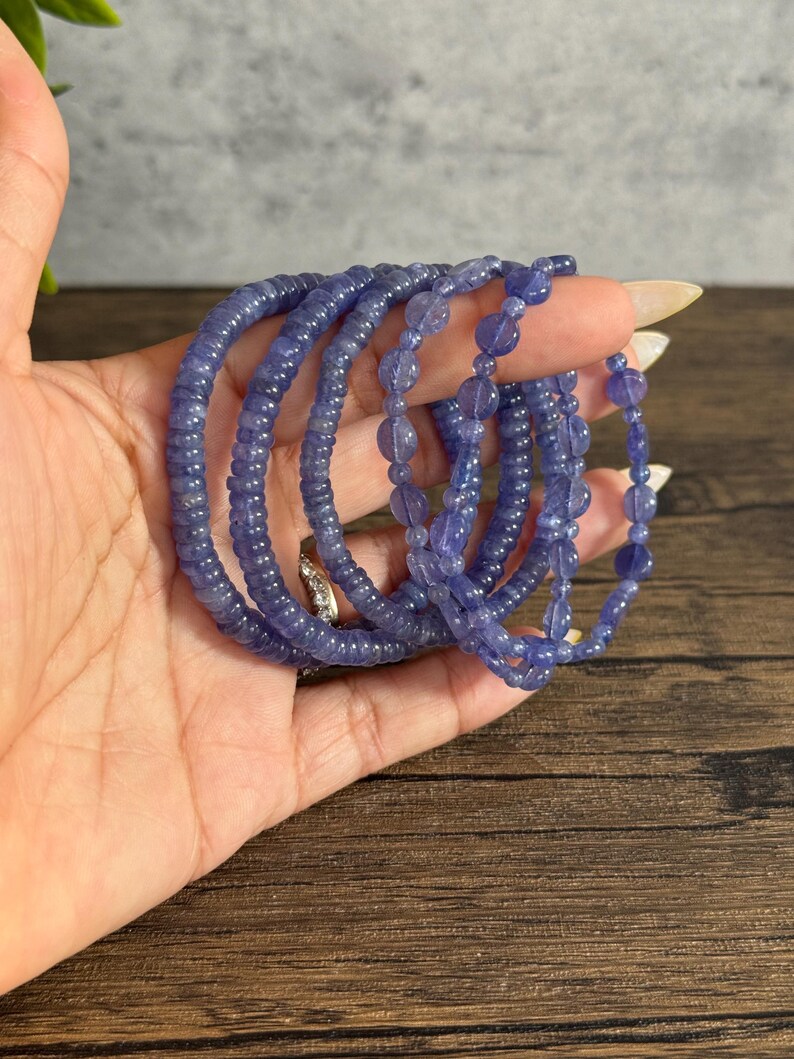 Puede incluir: Un conjunto de seis pulseras de piedras preciosas azules, cada una con un tama&ntilde;o y estilo de cuentas diferente. Las pulseras est&aacute;n apiladas una encima de la otra en una mano.