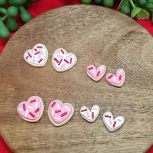 Op de afbeelding: Een set van zes hartvormige koekjes versierd met roze en rode glazuur en sprinkles. De koekjes zijn gerangschikt op een houten oppervlak.