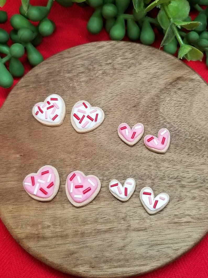 Op de afbeelding: Een set van zes hartvormige koekjes versierd met roze en rode glazuur en sprinkles. De koekjes zijn gerangschikt op een houten oppervlak.