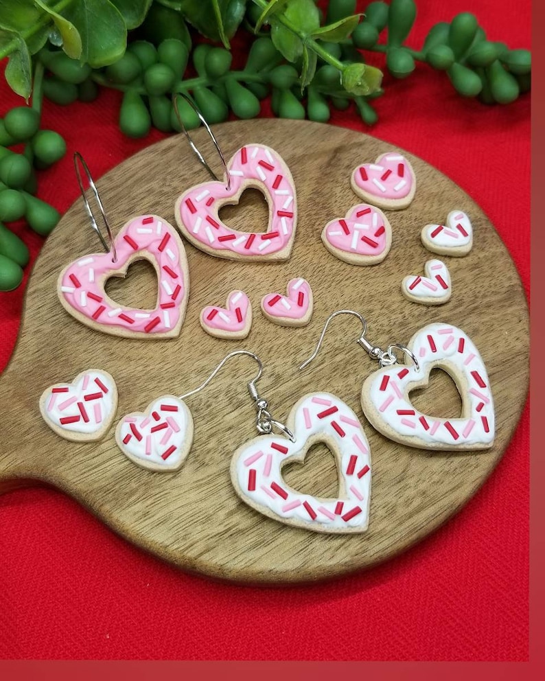 Op de afbeelding: Een set van vier paar hartvormige oorbellen met roze en witte frosting en rode en roze sprinkles. De oorbellen zijn gemaakt van polymer clay en zijn perfect voor Valentijnsdag.
