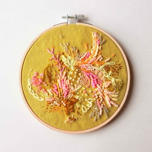 Textile abstract Wall art made out of Embroidery and Beads, shaped in a Embroidery Hoop, in yellowish andpinkish tones.