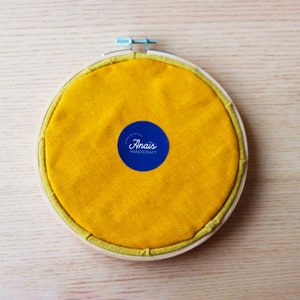 Back of the embroidery hoop with yellow fabric and name of the artist.