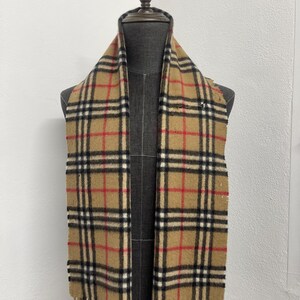 May include: A tan scarf with a classic plaid pattern in black, red, and white. The scarf is displayed on a mannequin and has fringed edges. The scarf is a classic accessory.