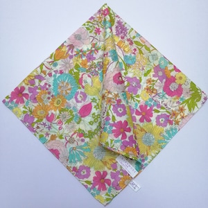 May include: A white cotton fabric with a floral print in shades of pink, yellow, green, and blue. The fabric features a variety of flowers, including roses, daisies, and lilies. The fabric is folded in half and has a label that reads "Intermode Liberty of London".
