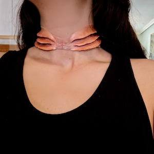 Puede incluir: Primer plano de una persona que lleva un top negro de tirantes con un collar de color carne de varias capas alrededor del cuello.