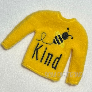 May include: A yellow long-sleeved sweater with the word "Kind" embroidered in black, along with a cartoon bee. The bee has black and yellow stripes. The sweater is made of a soft, fuzzy material.