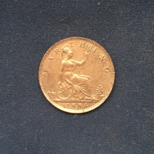 May include: A copper-coloured British half penny coin with the inscription "ONE HALF PENNY" and the year "1884" on the reverse side.