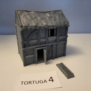May include: A gray, 3D printed model of a two-story building with a gabled roof and a door. The building has a wooden frame and stone walls. The model is labeled "TORTUGA 4".