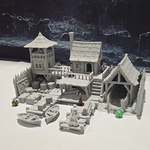 May include: A gray 3D printed miniature model of a waterfront building with a tower, a small house, and a boat shed. The model includes a variety of details, such as a fence, a dock, and a small figure.
