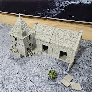 May include: A gray stone building with a tower and multiple windows. The building has a stone roof and is made of multiple pieces. A green and gold dice is in the foreground.
