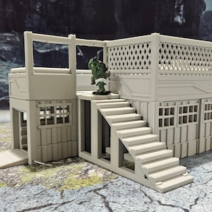 May include: A two-story white building with a wooden door, windows, and a balcony with a lattice railing. A small green figure stands on the balcony.
