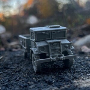May include: A gray toy truck with a flatbed, a cab with two windows, and a grill with a black mesh. The truck is sitting on a gravel surface.