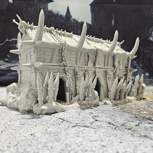 May include: A gray, detailed, miniature building with a pointed roof and a fence made of spikes. The building has a rough, textured surface and appears to be made of stone. The building has two doors and a window.