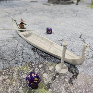 May include: A white miniature boat with a figure of a wizard in a pointed hat and a staff. The boat is docked at a post with a rope wrapped around it. There are two purple dice with gold numbers on a gray surface.