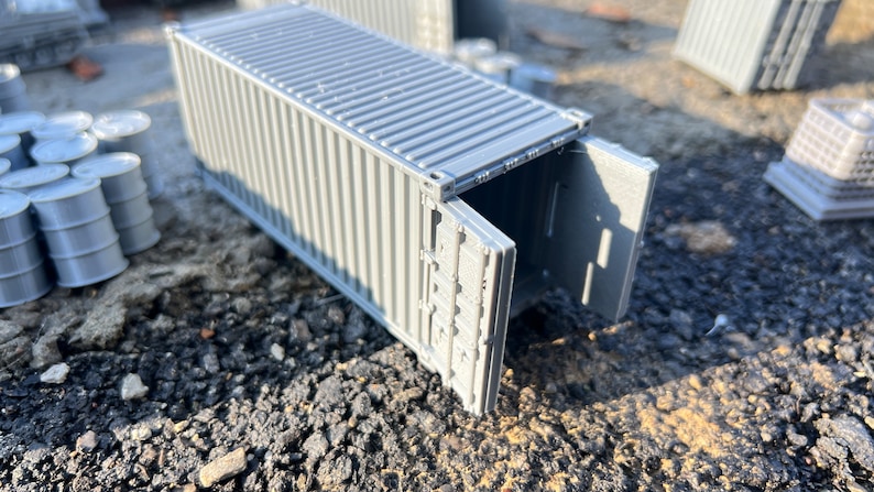 May include: A gray metal shipping container with the doors open. The container is sitting on a gray gravel surface.