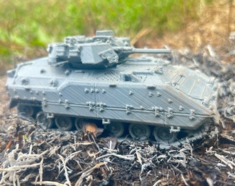 May include: A gray, detailed model of a military armored vehicle with a turret and tracks. The model is sitting on a bed of dry leaves and twigs.