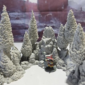 May include: A miniature fantasy landscape with gray trees and rock formations. A small, colorful figure with a red hat and staff stands in the center. The scene is designed for tabletop gaming or display.