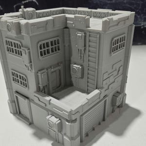 May include: A gray, multi-level, 3D printed building model with a flat roof and a variety of windows and doors. The building has a textured surface and appears to be made of concrete.