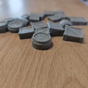 May include: A collection of small, gray miniature barrels and crates. The barrels have a wooden plank design on top, and the crates have a slatted design. The objects are scattered on a light brown wooden surface.