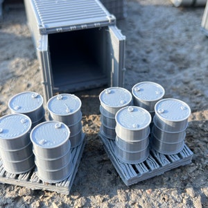 May include: Two pallets of gray plastic barrels, each pallet holding six barrels. The barrels are stacked two high. A gray shipping container with its doors open is in the background.