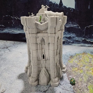 May include: A gray, stone-like tower with a cannon on top. The tower has a pointed roof and several windows. There are small green figures on the tower.