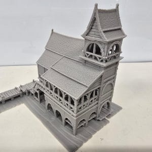 May include: A gray 3D printed miniature building featuring a multi-level structure with a tall tower, arched openings, textured roof shingles, and a wooden-style plank dock extending from the side, all rendered in a single solid monochromatic tone.