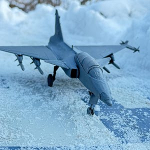 May include: A gray model airplane with a detailed design, sitting on a snowy surface.
