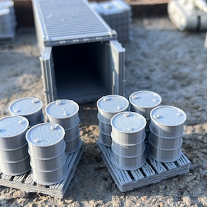 May include: A gray shipping container with its doors open, revealing a stack of gray barrels on wooden pallets. The barrels are arranged in two rows of four, with the container in the background.
