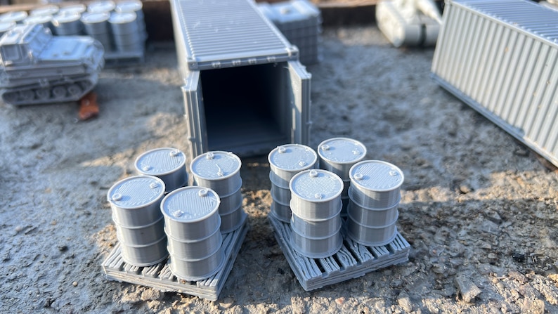 May include: A gray shipping container with its doors open, revealing a stack of gray barrels on wooden pallets. The barrels are arranged in two rows of four, with the container in the background.
