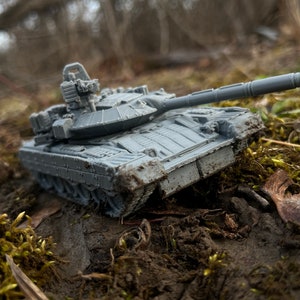 May include: A gray toy tank model with a long barrel and detailed features, sitting on a bed of green moss and dirt.