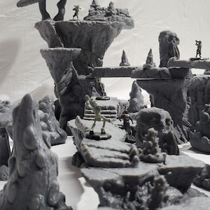 May include: A gray 3D printed miniature terrain set with a mushroom-shaped rock formation, a skeletal figure, and other rock formations.