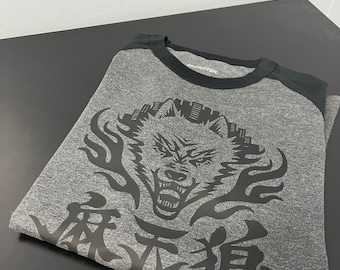 May include: A gray and black long-sleeve t-shirt with a black wolf graphic and Japanese characters. The wolf is surrounded by flames and the characters are below the wolf.