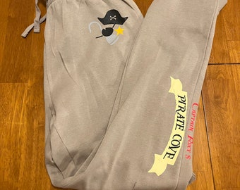 May include: Gray sweatpants with a pirate design on the left leg and the text "Captain Foxy's Pirate Cove" on the right leg.