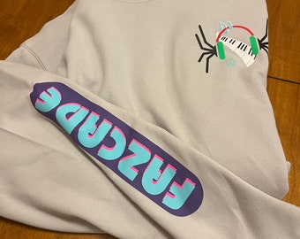 May include: Gray hooded sweatshirt with a graphic of a spider wearing headphones and holding a keyboard. The text "FASCADE" is printed on the sleeve in blue, pink, and purple.