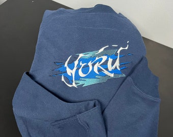 May include: A navy blue long-sleeved shirt with a white embroidered graphic of the word "YORK" in a stylized font with blue and green accents.