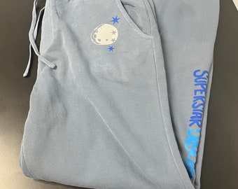 May include: Blue sweatpants with a moon and stars graphic on the left leg and the text "SUPERSTAR DISC" on the right leg.