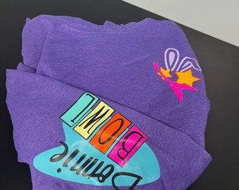 May include: Purple hoodie with a blue and white graphic that says "Bennie" and "BOWL" in colorful letters. The graphic is on the left side of the hoodie. There is a pink bunny rabbit with a yellow star on the right side of the hoodie.