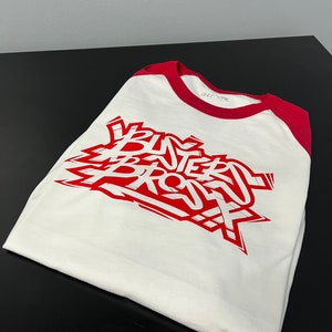 May include: White and red baseball tee shirt with the words "BUTTERED BROS" printed in red on the front.
