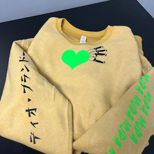 May include: A mustard yellow sweatshirt with a green heart and black knives on the front. The left sleeve has black Japanese text that reads "デイジー・デイジー". The right sleeve has green text that reads "ON THE WAY DOWN YOU WON'T FEEL SO BAD".