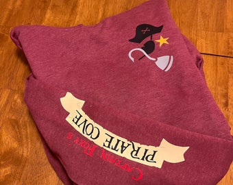 May include: A maroon hoodie with a white graphic of a pirate's hat, hook, and eye patch. The text "Captain Foxy's Pirate Cove" is printed on the sleeve in a white banner.